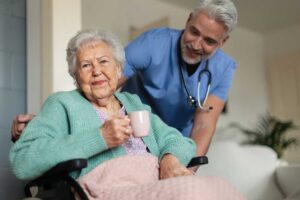 Two seniors and a caregiver sharing a gentle conversation in a brightly lit assisted living common area.